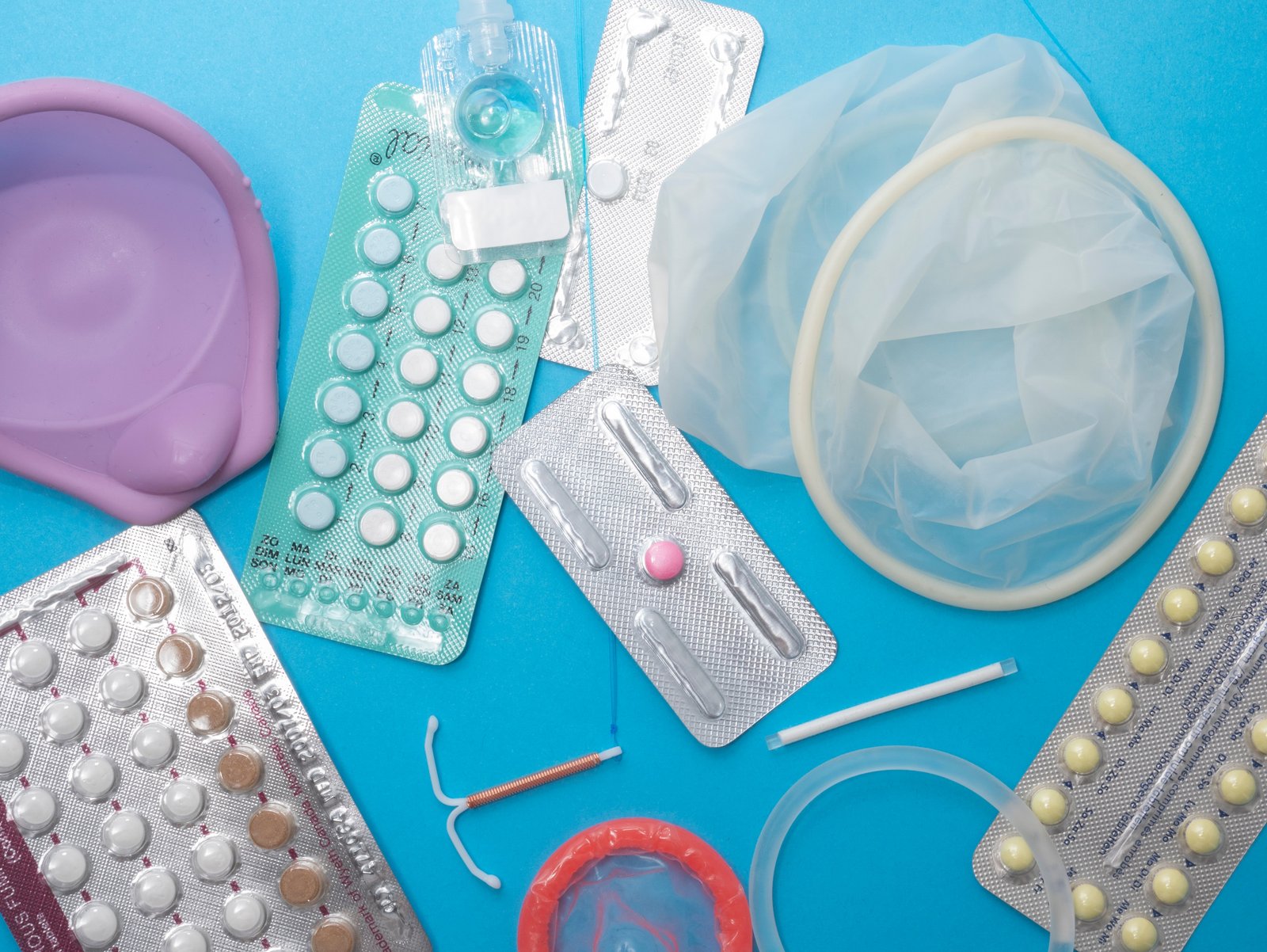 Modré pozadie, na ktorom ležia rôzne hormonálne a bezhormonálne antikoncepčné prostriedky pre ženy