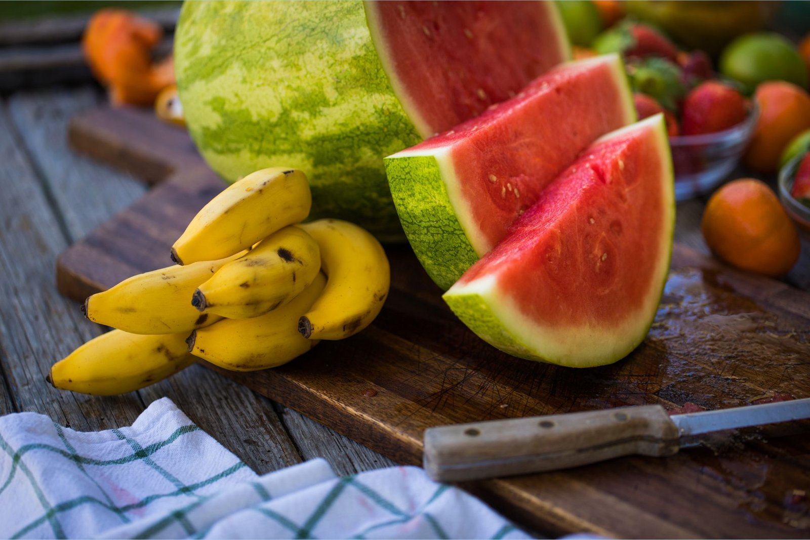 Banány bohaté na draslík ležia na doske na krájanie vedľa plátkov melóna bohatého na L-citrulín